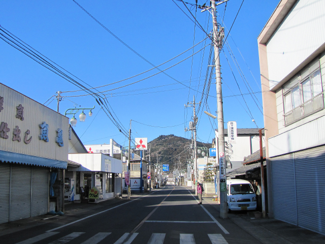 駅前からやや左手方向に真っすぐ伸びる道。冬の空は真っ青。正面にはこれから登る愛宕山が見えています。